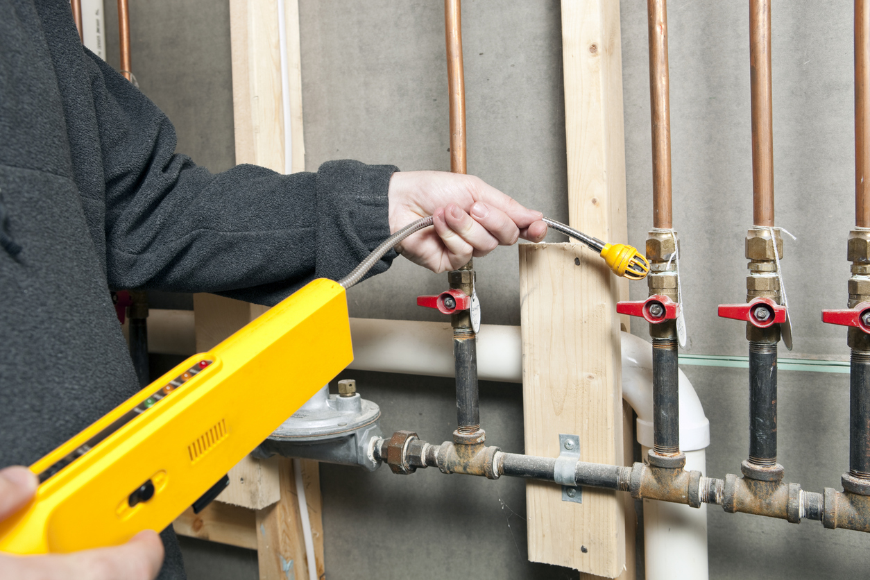 A technician is using a leak detector near a set of house gas lines.