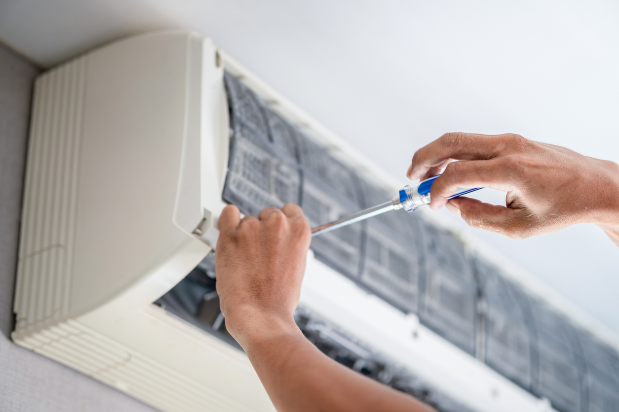 HVAC technician performing an AC tune-up on a wall-mounted air conditioning unit.