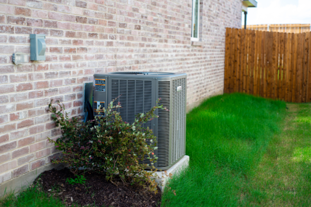 Outdoor HVAC unit and wall mounted electrical boxes installed alongside modern brick home